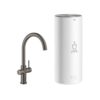 Een Grohe Red 3-in-1 C-uitloop Mat Donkergrijs L-vormige boiler keukenkraan met een gebogen uitloop wordt getoond naast een hoge, cilindervormige witte GROHE Red waterfilterunit met een kopje en stoompictogram op de voorkant.